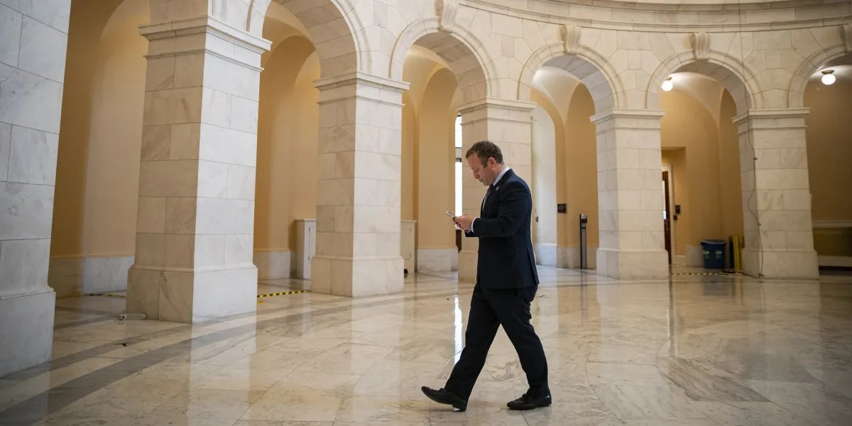 Businessman in a dark suit walks through a marble arched hall while looking at his phone.