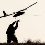 Silhouette of a person on a grassy hill launching a small airplane drone by a tethered launcher.