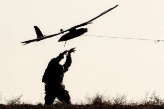 Silhouette of a person on a grassy hill launching a small airplane drone by a tethered launcher.