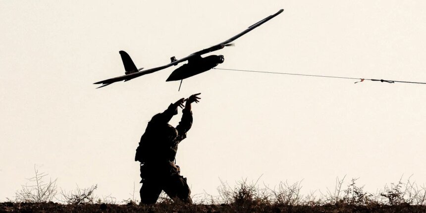 Silhouette of a person on a grassy hill launching a small airplane drone by a tethered launcher.