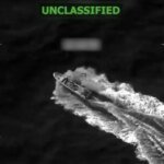 Night-vision style image of a fast-moving vessel carving a wake through dark water, with 'UNCLASSIFIED' in green text at the top.