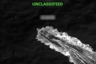 Night-vision style image of a fast-moving vessel carving a wake through dark water, with 'UNCLASSIFIED' in green text at the top.